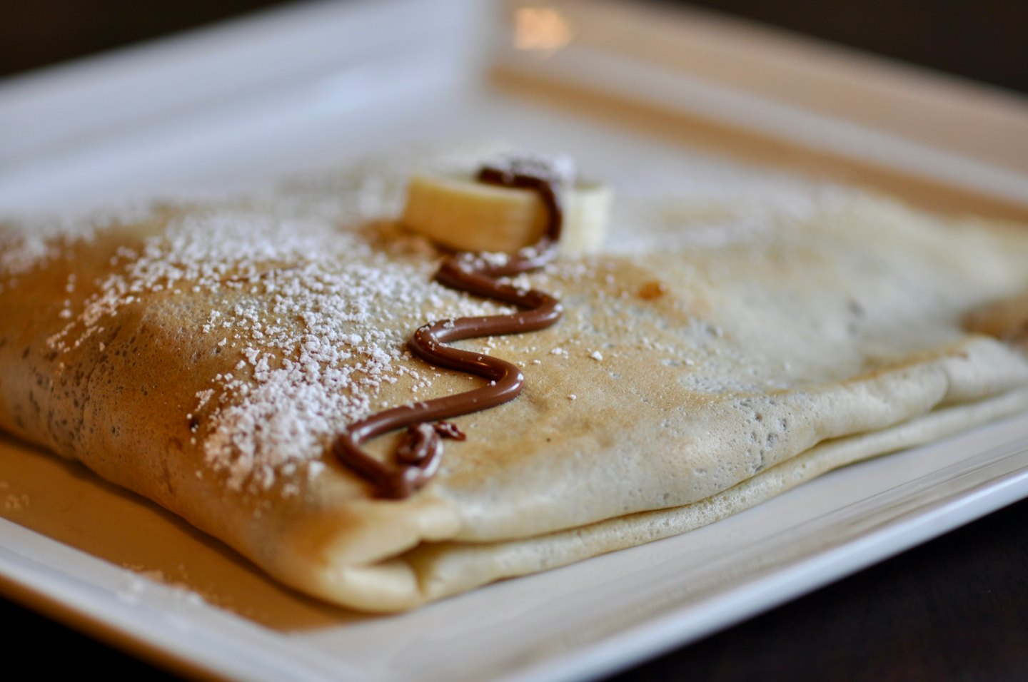 A golden crepe dusted with powdered sugar and chocolate sauce.