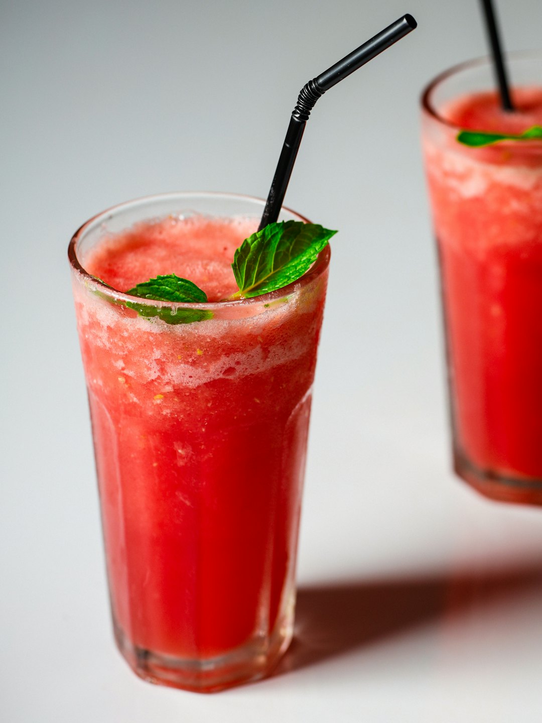 Two red fruit smoothies with mint garnishes on a table.