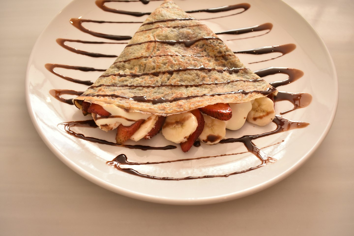 Crepe filled with fruit and cream, drizzled with chocolate sauce.