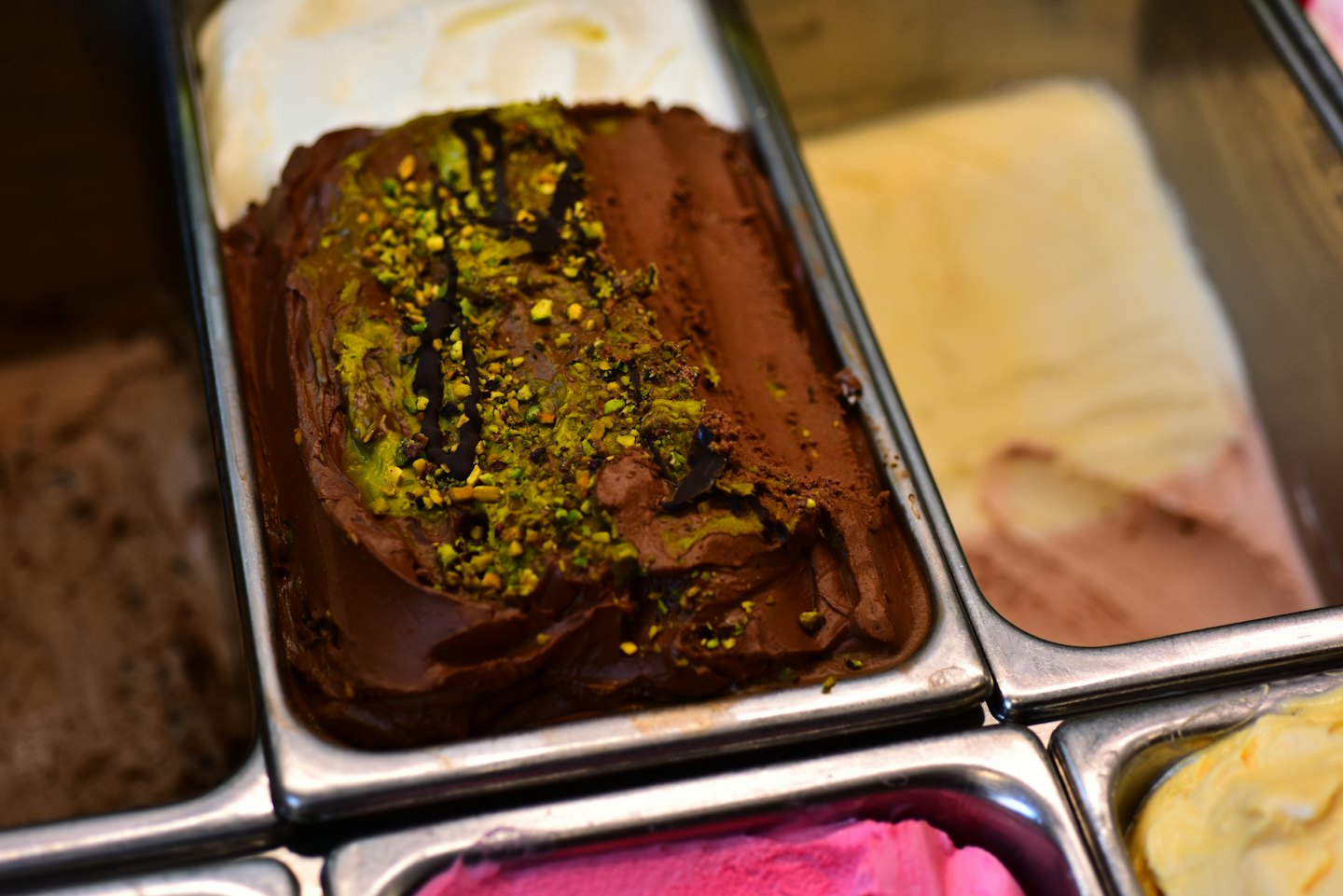 Assorted artisan gelato flavors displayed in metal serving tubs.